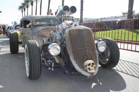 1998 Ford Crown Victoria - A heavily modified hot rod with a prominent skull ornament on its front grille is parked outdoors.