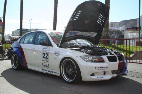 1998 Ford Crown Victoria - Modified BMW sedan with custom graphics and aftermarket wheels, hood open at an outdoor event.