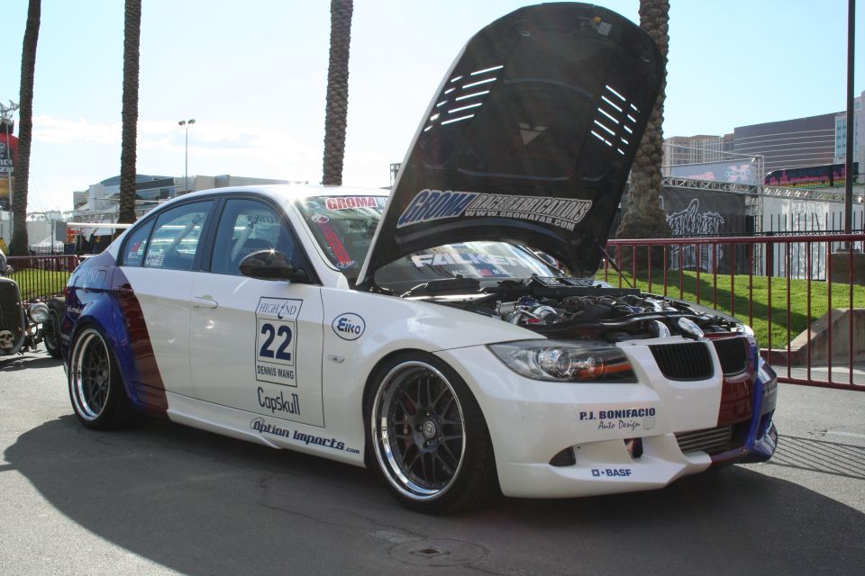 White BMW sedan with custom paint on rear quarter panels, hood open showing engine. Decals include 'HIGHLAND 22', 'GROMA', and 'P.J. BONIFACIO Auto Design'