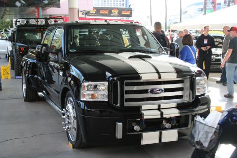 1998 Ford Crown Victoria - A black Ford F-Series Super Duty truck with racing stripes is displayed outdoors, with other vehicles and people around.