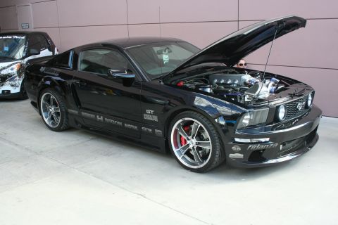 1998 Ford Crown Victoria - This black Ford Mustang GT displays its engine and custom wheels with the hood open.