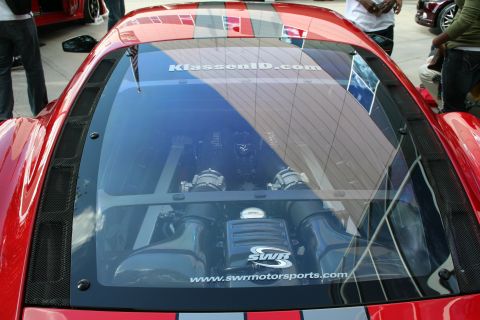 1998 Ford Crown Victoria - A red sports car's engine bay is visible through the rear glass, with website text on the window.