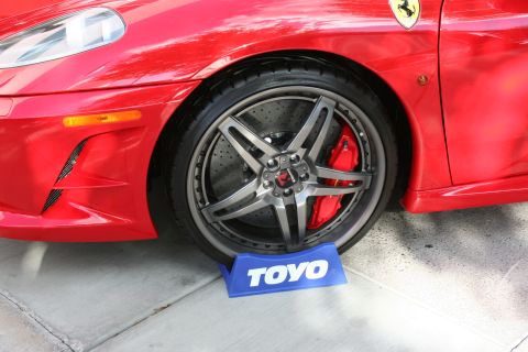 1998 Ford Crown Victoria - Close-up of a red sports car's front wheel, custom rims, red brake calipers, and a TOYO tire stand.