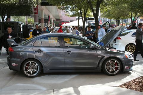 1998 Ford Crown Victoria - A gray Mitsubishi Lancer Evolution is parked outside with other vehicles and people around.