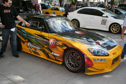 1998 Ford Crown Victoria - A customized yellow and black sports car with numerous racing decals is displayed at an outdoor event.