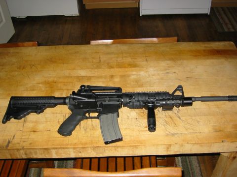 1996 Ford Bronco - A black rifle with a collapsible stock and a vertical foregrip rests on a wooden surface.