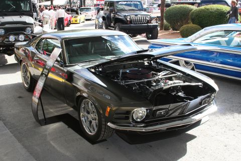 1998 Ford Crown Victoria - A dark green 1970 Ford Mustang coupe is displayed with its hood open, revealing the engine compartment, parked outdoors with other vehicles.