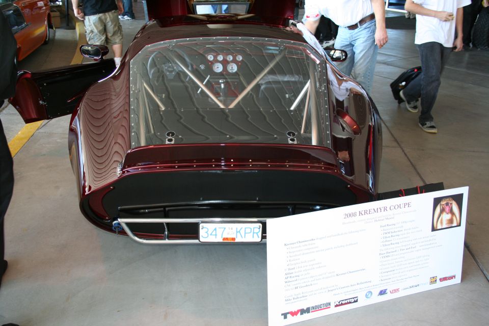 Custom coupe with exposed roll cage, gauges visible through rear window, and a sign identifying it as a 2008 Kremyr Coupe