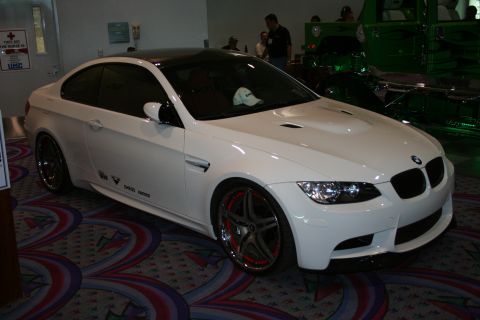 1998 Ford Crown Victoria - A white BMW coupe with a black roof and custom wheels is displayed indoors, with another green vehicle visible in the background.