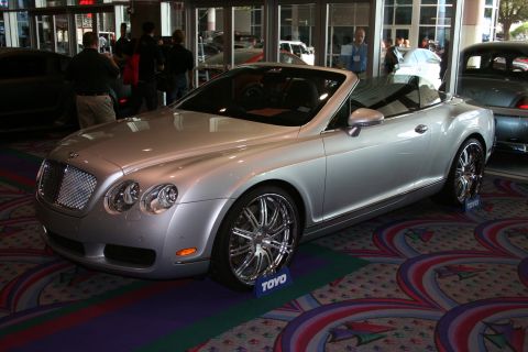 1998 Ford Crown Victoria - A silver Bentley convertible is displayed indoors with custom chrome wheels and a prominent grille.