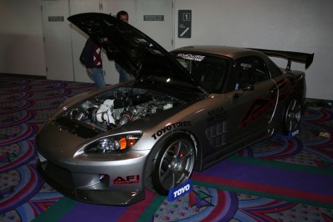 1998 Ford Crown Victoria - A modified silver sports car is displayed with its hood open, revealing the engine and turbocharger, adorned with various racing decals.