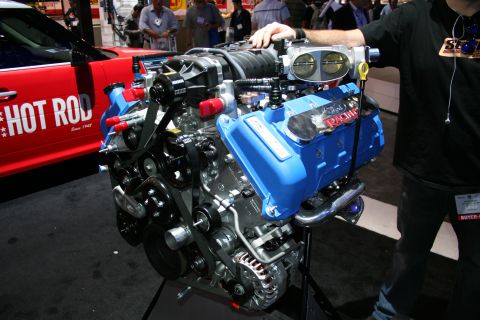 1998 Ford Crown Victoria - A blue Ford Racing engine is displayed, with the words "HOT ROD" visible on a red car in the background.