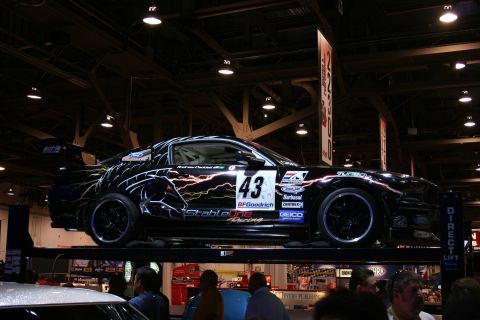 1998 Ford Crown Victoria - Customized Ford Mustang race car with lightning bolt graphics and sponsor decals is displayed on a lift.