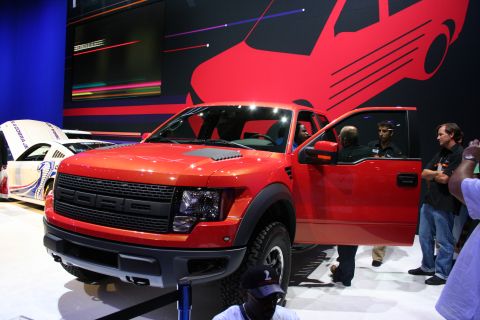 1998 Ford Crown Victoria - A red Ford F-150 Raptor is displayed with its door open, alongside another vehicle.