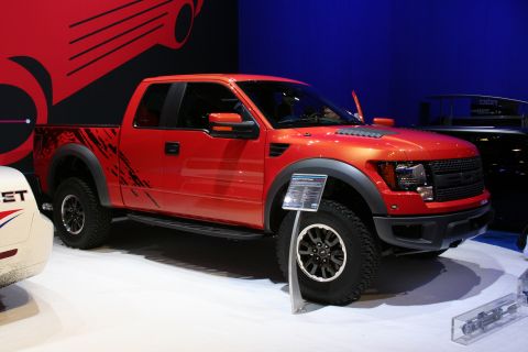 1998 Ford Crown Victoria - A red Ford F-150 Raptor pickup truck is displayed indoors, a prominent grille and aggressive styling.