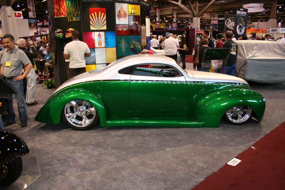 Green and white custom coupe with chrome wheels, lowered suspension, and pinstripe details. It's at an indoor car show