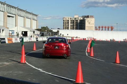 1998 Ford Crown Victoria - A red Lexus sedan navigates a course marked by cones and flags, with buildings in the background.
