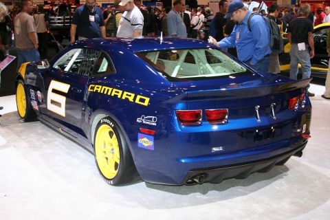 1998 Ford Crown Victoria - A blue race car with yellow accents and racing decals is displayed indoors.