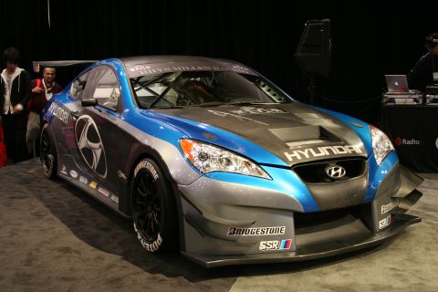 1998 Ford Crown Victoria - A Hyundai Genesis Coupe race car is displayed indoors with sponsors logos visible on its body.