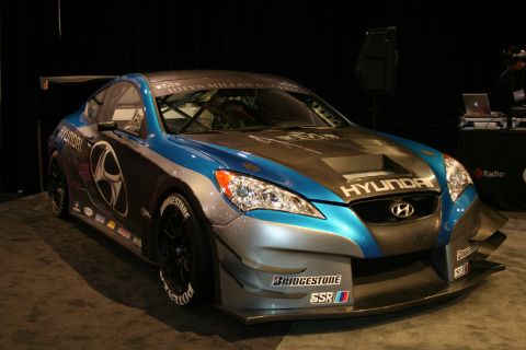 1998 Ford Crown Victoria - A Hyundai Genesis race car is displayed indoors with various sponsor decals on its body.