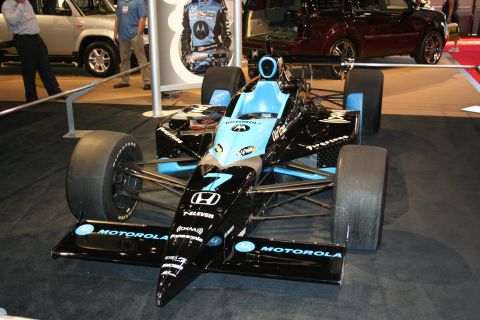 1998 Ford Crown Victoria - A race car with prominent sponsor decals is displayed indoors, with other vehicles visible in the background.