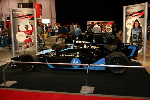 1998 Ford Crown Victoria - A black and blue racing car with sponsor logos is displayed indoors.