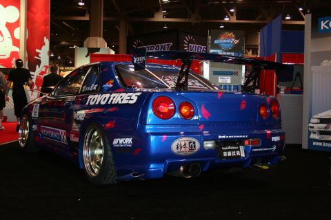 1998 Ford Crown Victoria - A heavily modified blue sports car with a prominent rear spoiler and numerous sponsor decals is displayed indoors.
