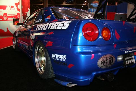 1998 Ford Crown Victoria - Modified blue sports car with racing decals and aftermarket wheels displayed indoors.