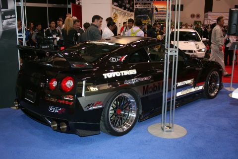 1998 Ford Crown Victoria - A modified black Nissan GT-R is displayed indoors with other vehicles and people around.
