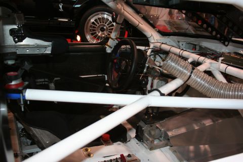 1998 Ford Crown Victoria - Interior view of a race car, showing the roll cage and driver's seat. A GT 500 is visible in the background.