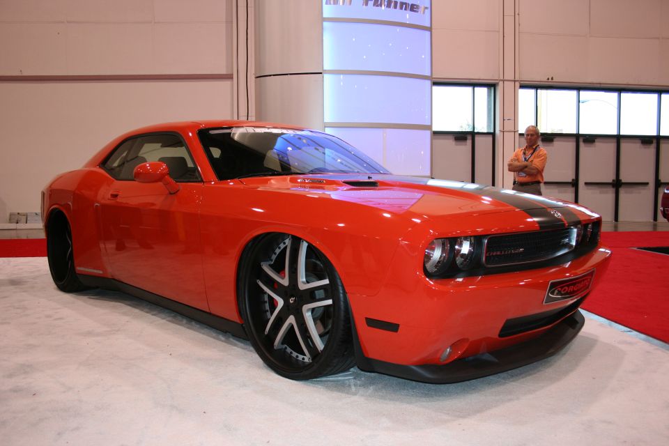 Orange Dodge Challenger with black racing stripes and custom rims, parked indoors