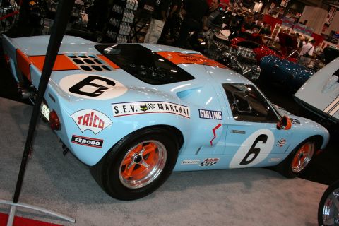 1998 Ford Crown Victoria - Light blue Ford GT40 race car with orange stripes and number 6 on the side, seen at a car show.