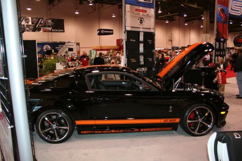 1998 Ford Crown Victoria - Black 2007 Ford Mustang Shelby GT500 on display with hood open at an auto show.
