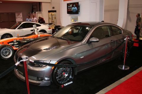 1998 Ford Crown Victoria - A gray BMW 3 Series Coupe is displayed indoors next to a white Porsche and a race car.
