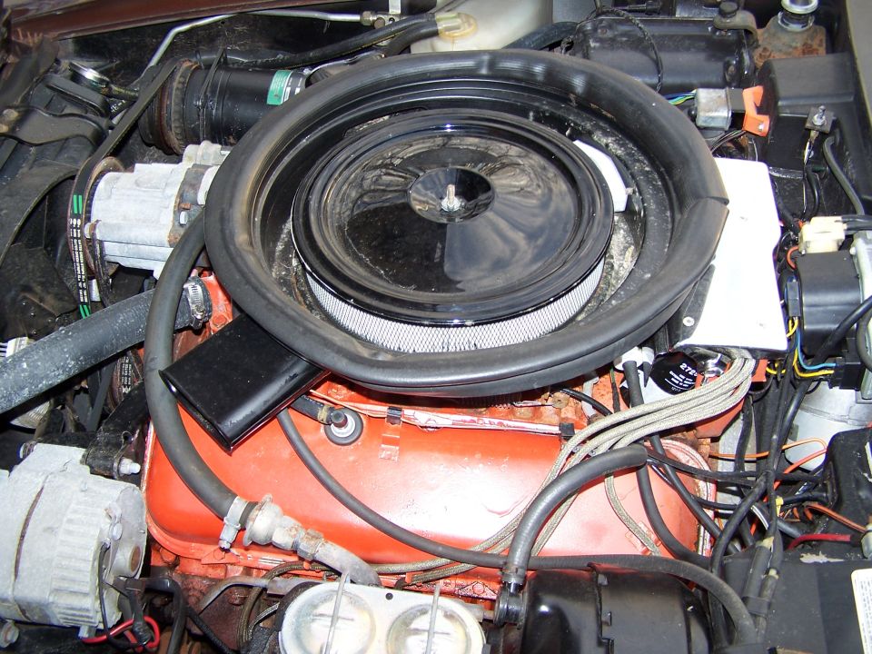 Engine bay with orange V8 engine block, black air cleaner assembly, and alternator