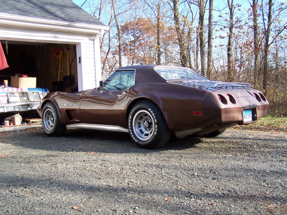 Brown 1975 Chevrolet Corvette parked in gravel driveway next to garage