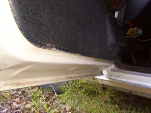 1991 Ford LTD Crown Victoria - Close-up view of a car's interior door sill, revealing wear and tear and the surrounding environment.