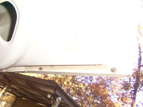 1991 Ford LTD Crown Victoria - Close-up view of a white car door's lower edge, revealing mounting hardware and a rustic corrugated roof structure.