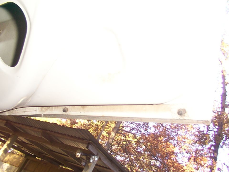 White car door edge with visible bolts and a corrugated metal roof in the background