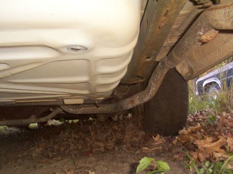1991 Ford LTD Crown Victoria - The underside of a car reveals a rusty exhaust system and a tire, with another vehicle partially visible.