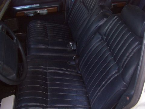 1991 Ford LTD Crown Victoria - The interior of a car shows dark vinyl seats with white stitching and wood trim on the dashboard.
