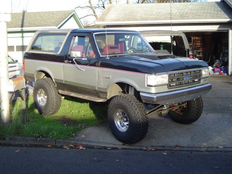 1989 Ford Bronco - This lifted Ford Bronco, with its distinctive two-tone paint and red interior, is parked in a residential driveway.