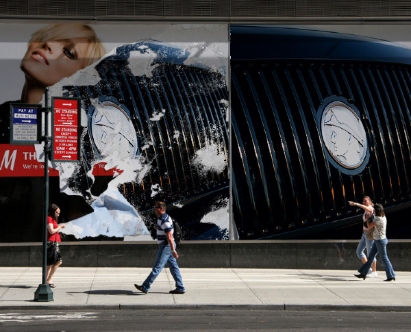 Torn billboard showing a car grille and a woman's face, with people walking on a sidewalk