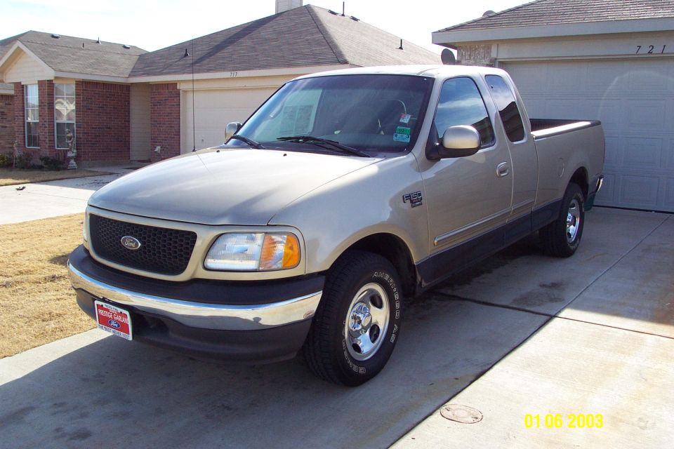 Tan Ford F-150 extended cab pickup, front 3/4 view, parked in driveway of brick house