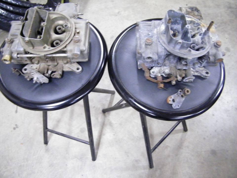 Two carburetors displayed on black stools