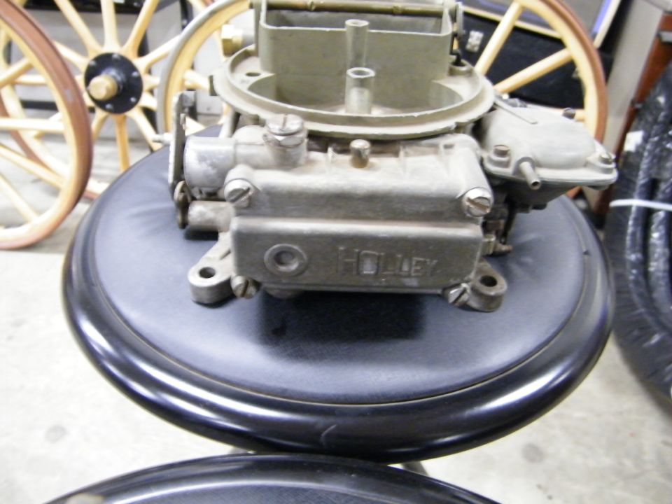 Holley carburetor on a stool, with old-fashioned wooden wheels in background