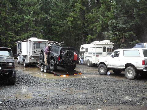 1991 Ford Bronco - Multiple Ford Broncos and RVs are gathered in a wooded area on a rainy day.