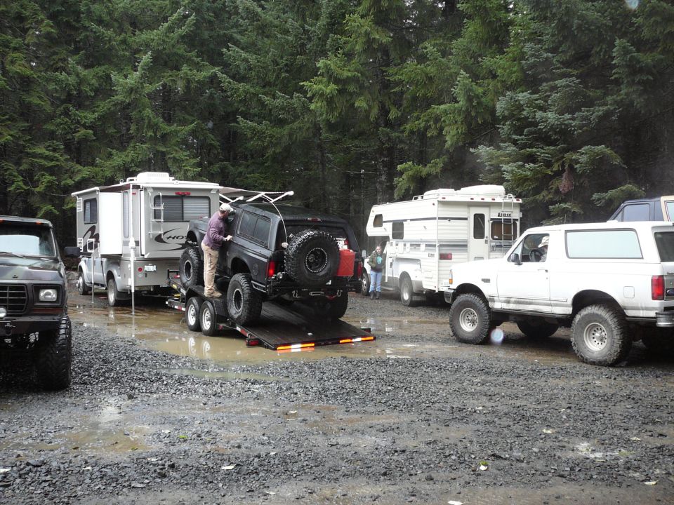 Black Ford Bronco on a trailer, being loaded, with a white Ford Bronco and RVs in the background