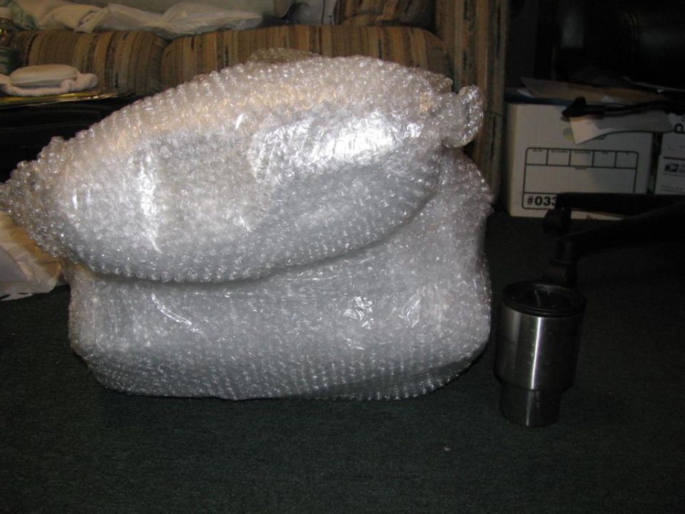 Engine intake part wrapped in bubble wrap next to a metal cylinder