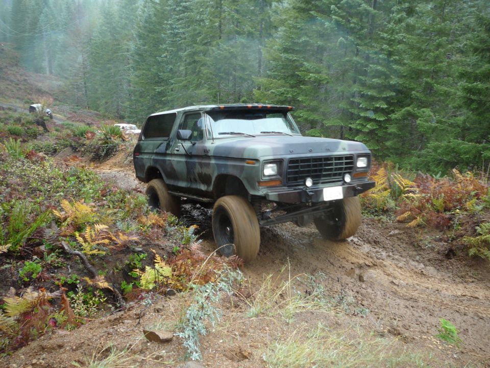 Camouflaged Ford Bronco climbing a muddy hill, another vehicle visible in background